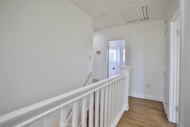 hallway featuring visible vents, light wood finished floors, an upstairs landing, and baseboards