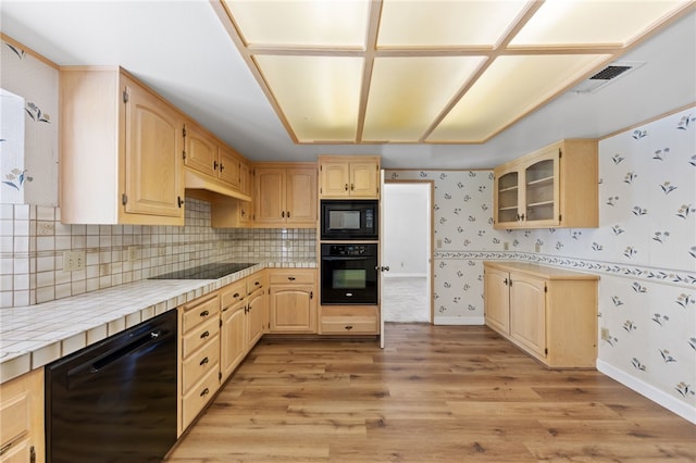 kitchen with light wood-style floors, light brown cabinetry, black appliances, glass insert cabinets, and wallpapered walls