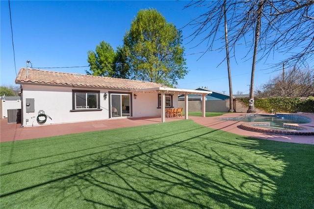 rear view of property featuring a patio, an in ground hot tub, a tile roof, a lawn, and stucco siding