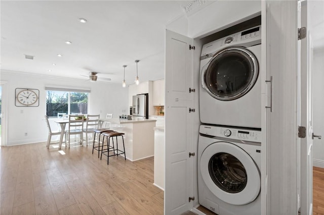 clothes washing area featuring light wood-type flooring, stacked washer and clothes dryer, baseboards, and laundry area