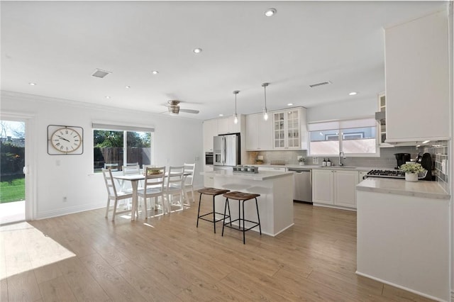 kitchen with a center island, appliances with stainless steel finishes, light wood-type flooring, decorative backsplash, and a kitchen bar