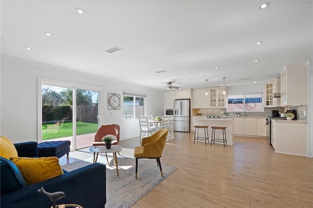 living room featuring light wood-type flooring, visible vents, ornamental molding, and recessed lighting