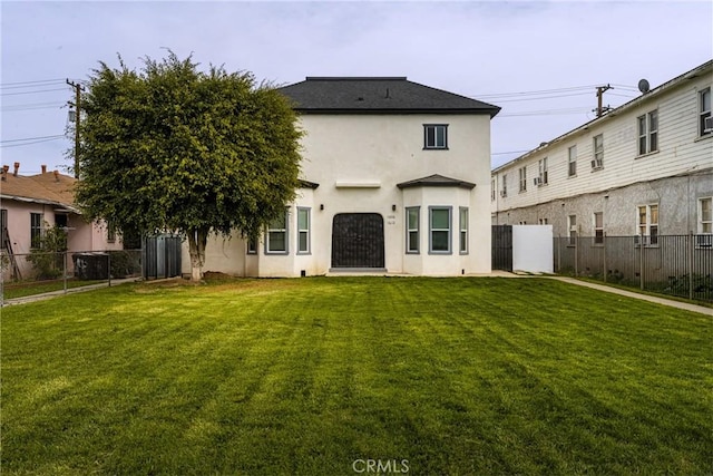 back of house with stucco siding, fence, and a yard