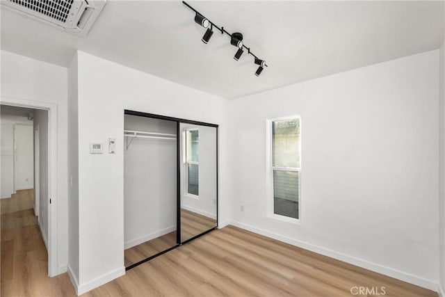 unfurnished bedroom with visible vents, baseboards, a closet, light wood-type flooring, and rail lighting