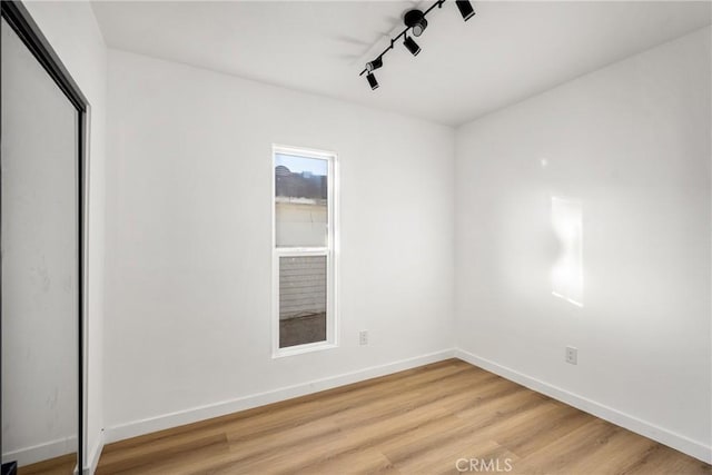 spare room with rail lighting, baseboards, and light wood finished floors