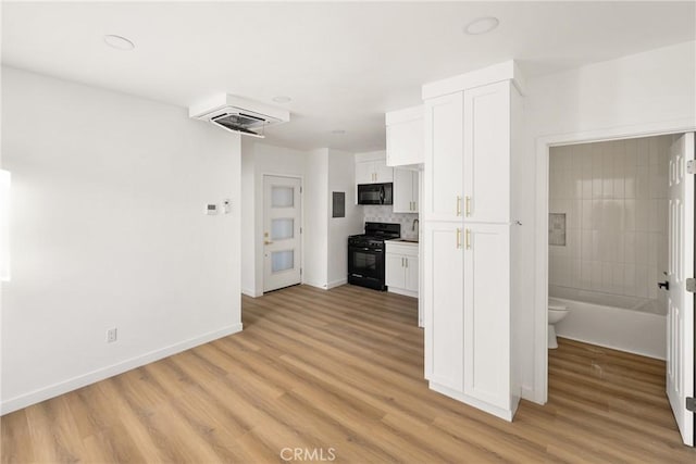 kitchen featuring light wood-style floors, white cabinets, a sink, black appliances, and baseboards