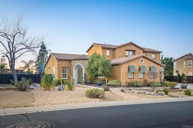 mediterranean / spanish-style home featuring stucco siding, fence, and a tiled roof