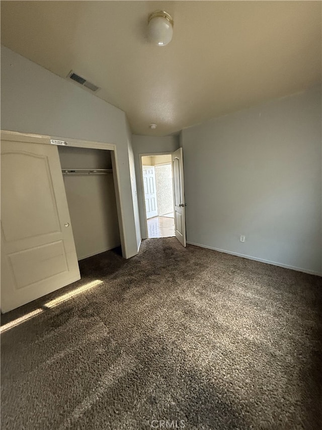 unfurnished bedroom with dark carpet, visible vents, and a closet