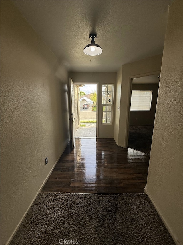 hall featuring baseboards, wood finished floors, a textured wall, and a textured ceiling