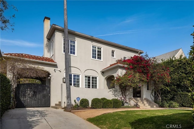 view of front facade featuring a chimney, stucco siding, a gate, driveway, and a front lawn