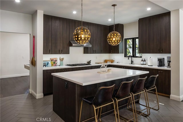 kitchen with light countertops, wall chimney range hood, dark brown cabinets, and a center island