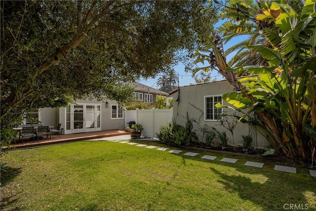 rear view of house featuring stucco siding, fence, a lawn, and french doors