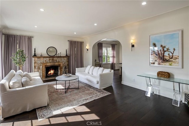 living area with arched walkways, recessed lighting, dark wood-type flooring, a warm lit fireplace, and baseboards