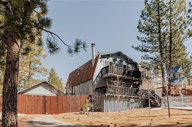 view of side of home featuring a shingled roof, fence, a balcony, and a gambrel roof