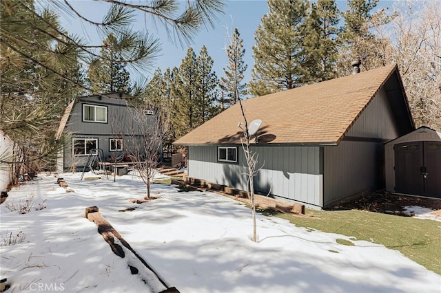 snow covered property with a patio area, an outdoor structure, and a shed