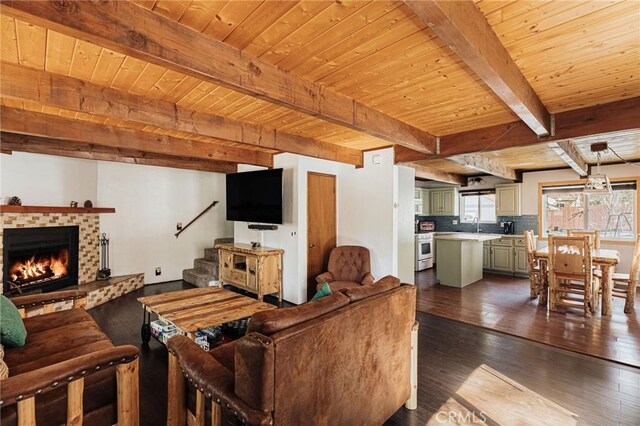 living area with dark wood-style floors, beam ceiling, a brick fireplace, wood ceiling, and stairs