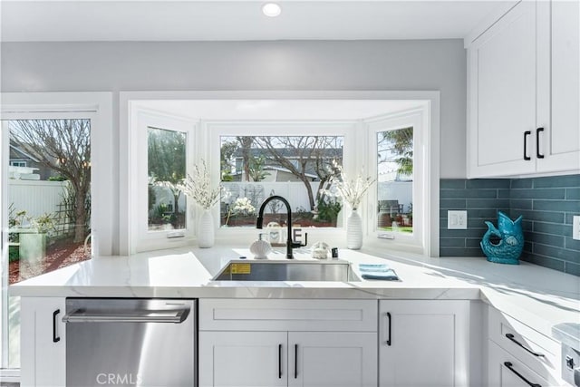 kitchen with decorative backsplash, dishwasher, light stone counters, white cabinetry, and a sink