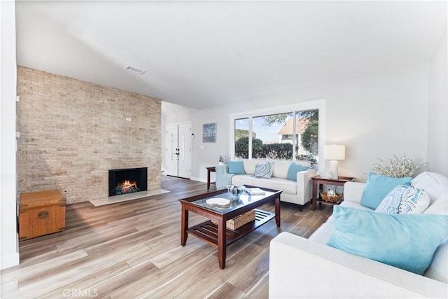 living area with light wood-type flooring, a large fireplace, visible vents, and baseboards