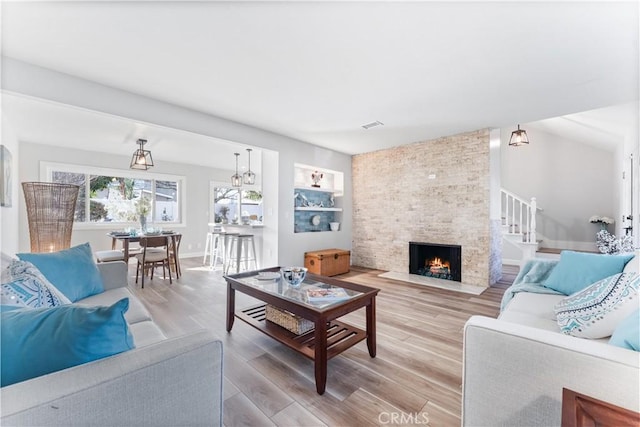 living area with a stone fireplace, visible vents, baseboards, stairs, and light wood-type flooring