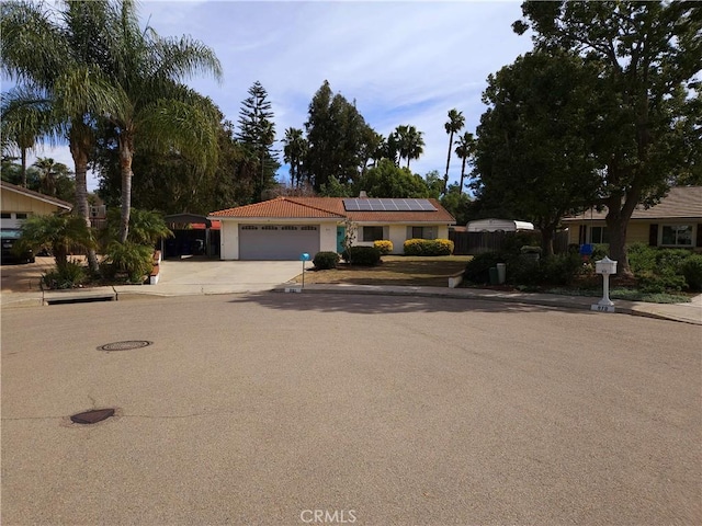 single story home with a garage, concrete driveway, fence, and roof mounted solar panels