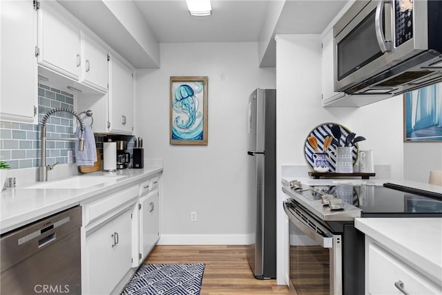 kitchen featuring stainless steel appliances, a sink, white cabinetry, light countertops, and tasteful backsplash