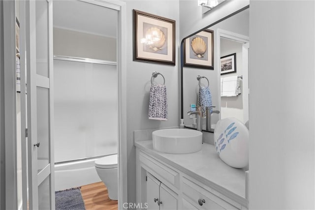 full bathroom with bath / shower combo with glass door, vanity, toilet, and wood finished floors