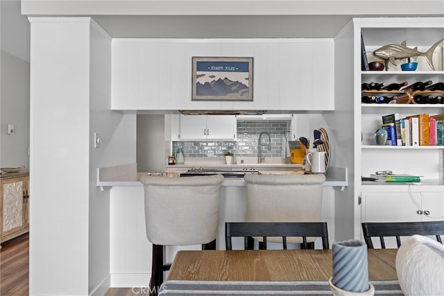 kitchen featuring backsplash, white cabinets, a sink, wood finished floors, and a kitchen bar