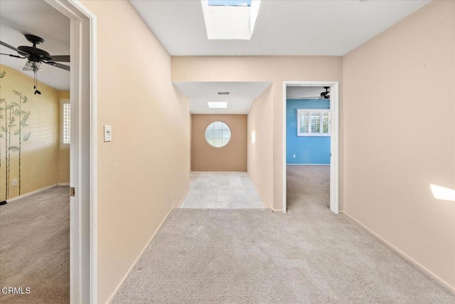 hall featuring a skylight, carpet, plenty of natural light, and baseboards