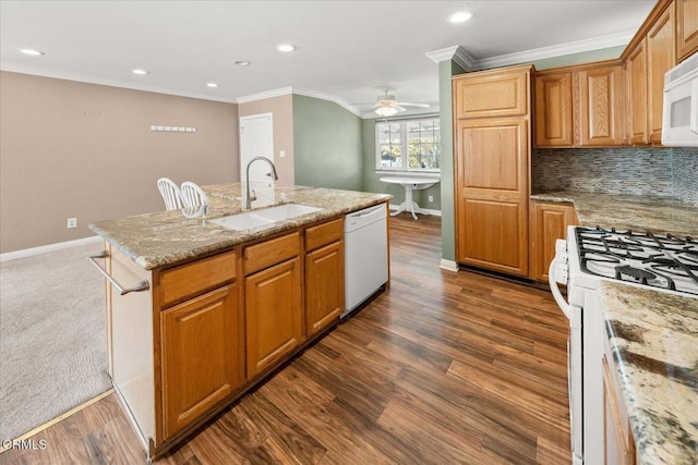 kitchen featuring crown molding, backsplash, a kitchen island with sink, a sink, and white appliances