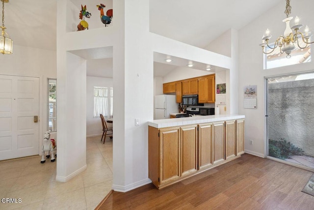 kitchen with light wood finished floors, stainless steel gas range oven, freestanding refrigerator, an inviting chandelier, and black microwave