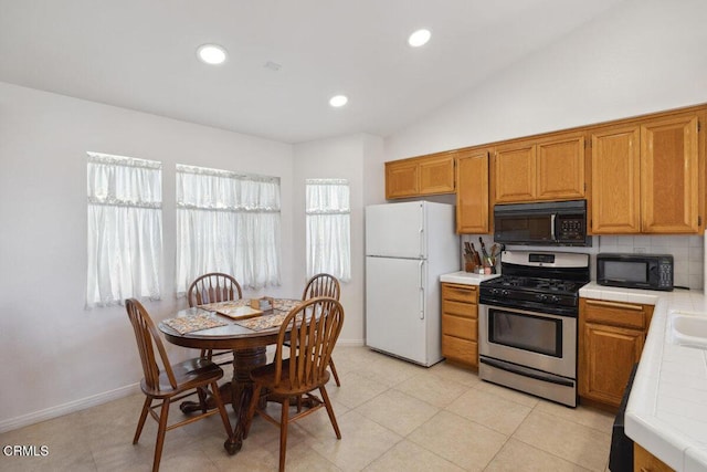 kitchen with black microwave, freestanding refrigerator, tile countertops, and stainless steel range with gas stovetop