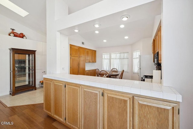 kitchen featuring recessed lighting, wood finished floors, vaulted ceiling with skylight, black microwave, and a peninsula