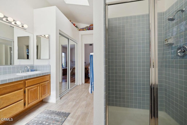 full bath featuring a stall shower, a skylight, wood finished floors, and vanity