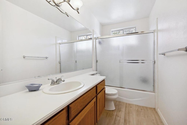 bathroom featuring toilet, wood finished floors, vanity, and enclosed tub / shower combo