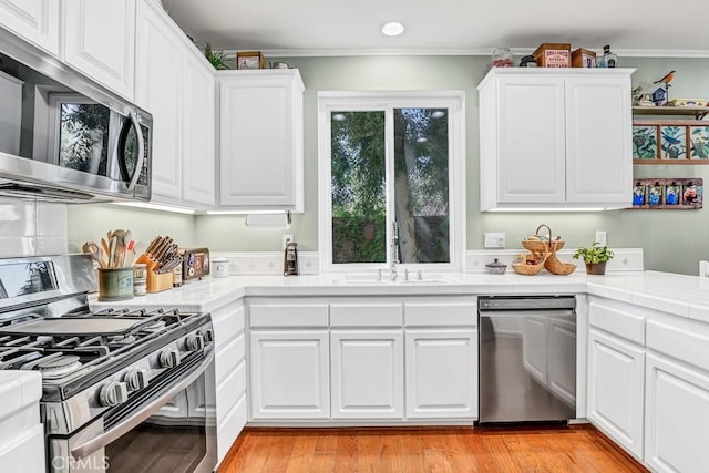 kitchen with tile counters, appliances with stainless steel finishes, light wood-type flooring, white cabinetry, and a sink