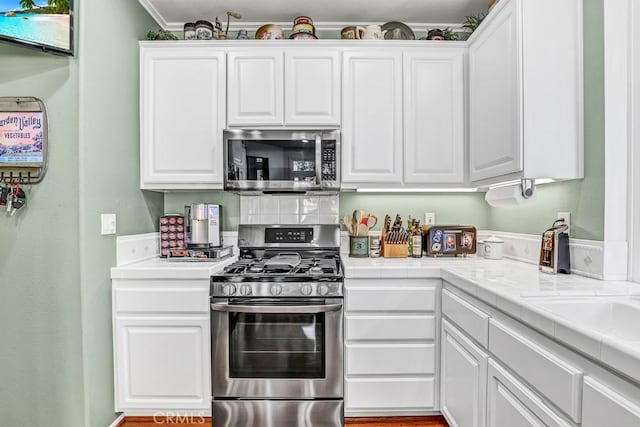 kitchen with tile countertops, white cabinetry, appliances with stainless steel finishes, and ornamental molding