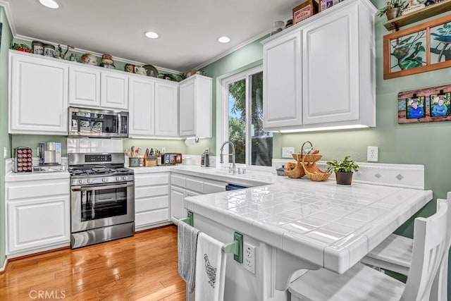 kitchen featuring light wood-type flooring, white cabinetry, appliances with stainless steel finishes, and tile counters