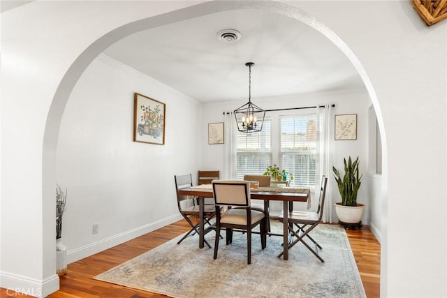 dining room featuring crown molding, light wood finished floors, visible vents, a chandelier, and baseboards