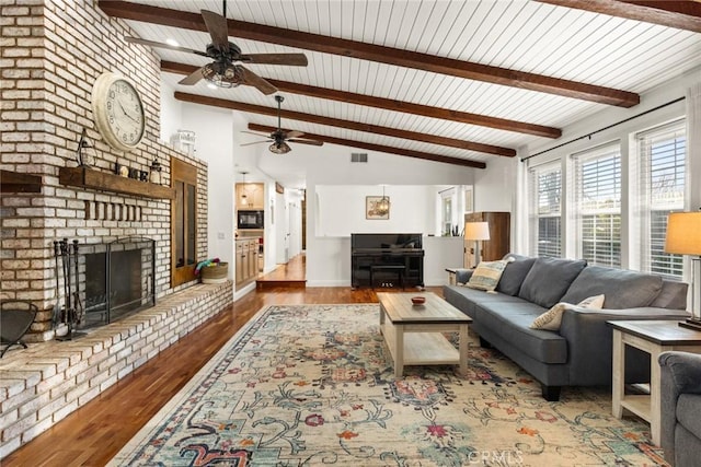 living area featuring a fireplace, visible vents, lofted ceiling with beams, wood finished floors, and baseboards