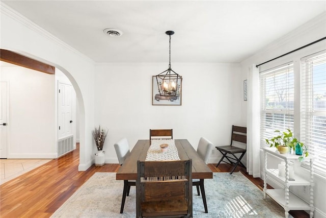 dining area featuring arched walkways, wood finished floors, visible vents, baseboards, and crown molding