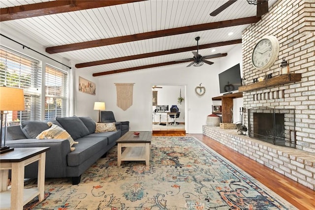 living area with a ceiling fan, a brick fireplace, vaulted ceiling with beams, and wood finished floors