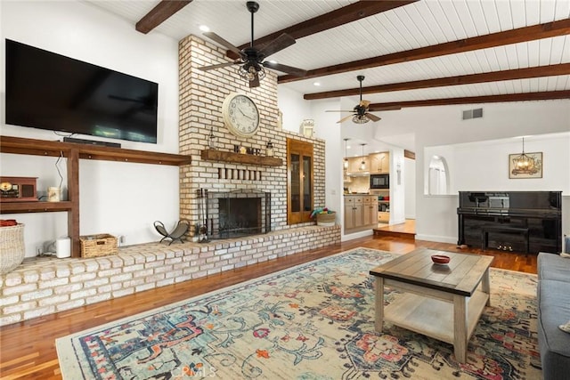 living room featuring a fireplace, visible vents, lofted ceiling with beams, ceiling fan, and wood finished floors