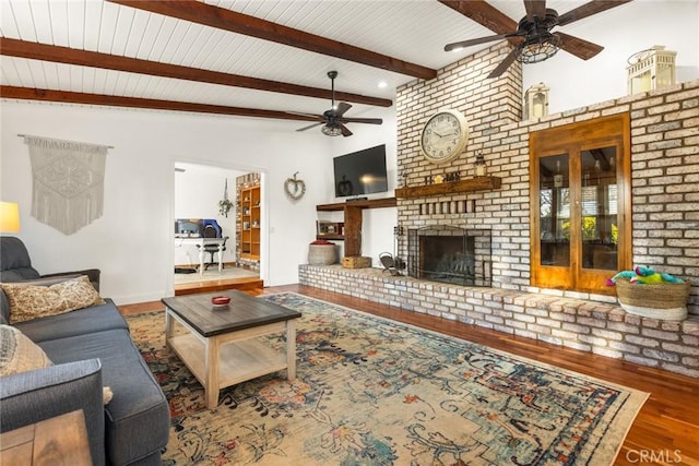 living area featuring a ceiling fan, a fireplace, beam ceiling, and wood finished floors