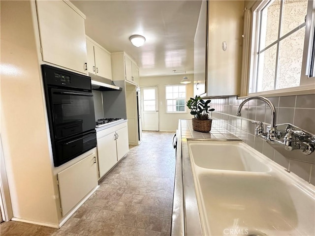 kitchen featuring gas cooktop, oven, under cabinet range hood, a sink, and white cabinets