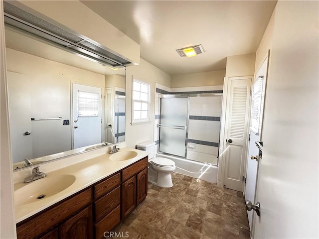 full bath featuring double vanity, shower / bath combination with glass door, a sink, and visible vents