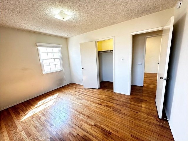 unfurnished bedroom with a closet, a textured ceiling, baseboards, and wood finished floors