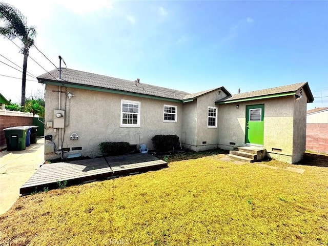 rear view of property featuring entry steps, a lawn, crawl space, fence, and stucco siding