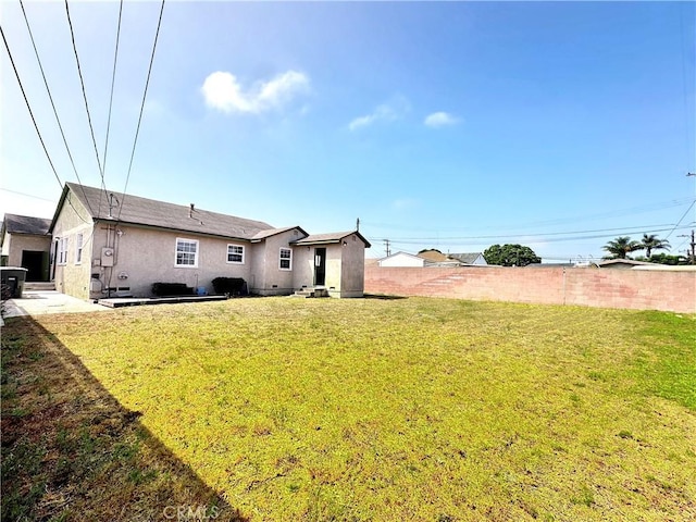 rear view of property featuring stucco siding, fence, and a yard