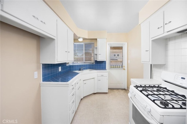 kitchen featuring tile countertops, backsplash, white cabinetry, a sink, and white range with gas stovetop