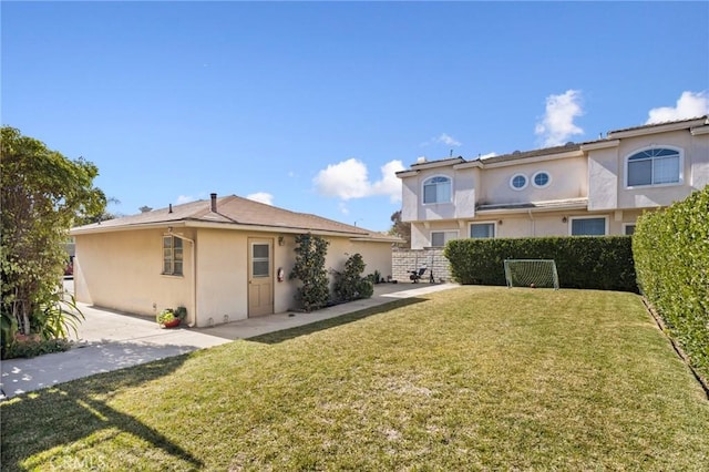 rear view of property featuring fence, a lawn, and stucco siding